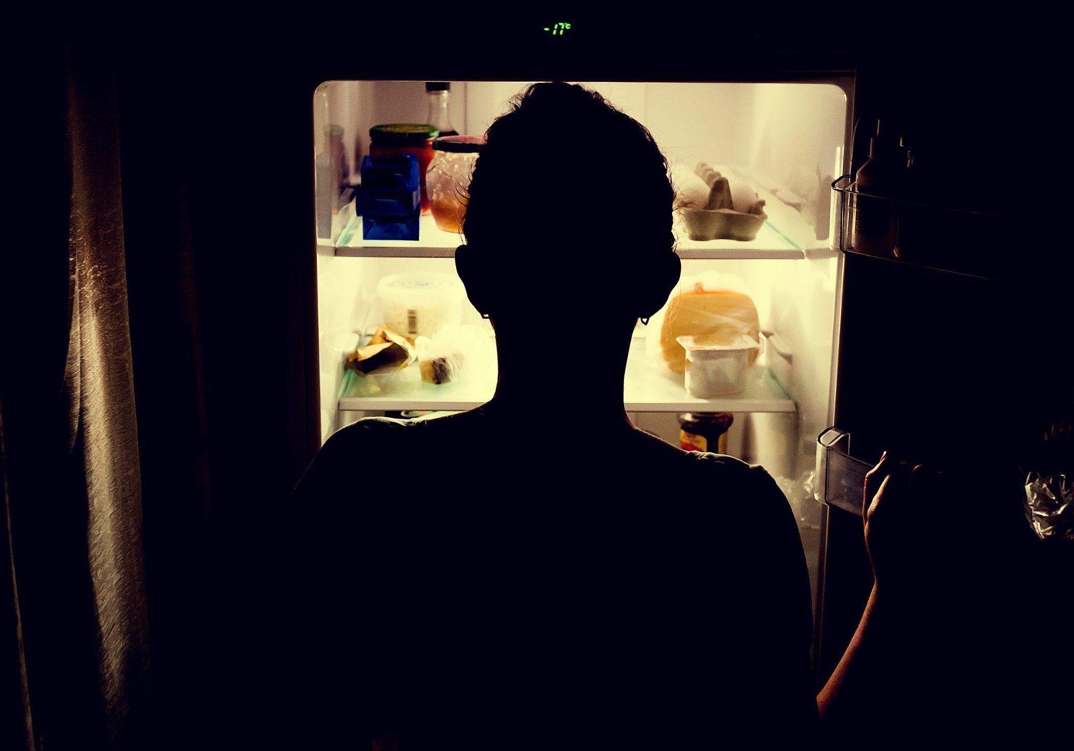 A sillhoutte of a person backlit by the light of a refrigerator, looking for something to eat