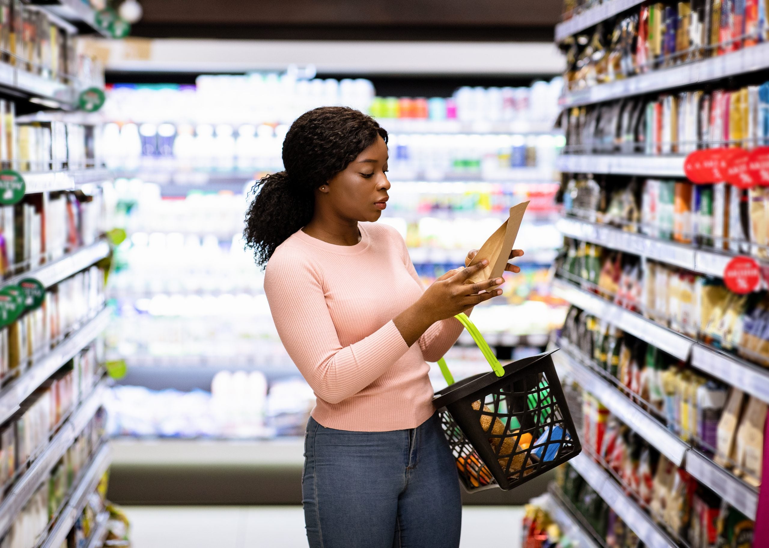A women grocery shopping and looking at the label on a package of food in her hand