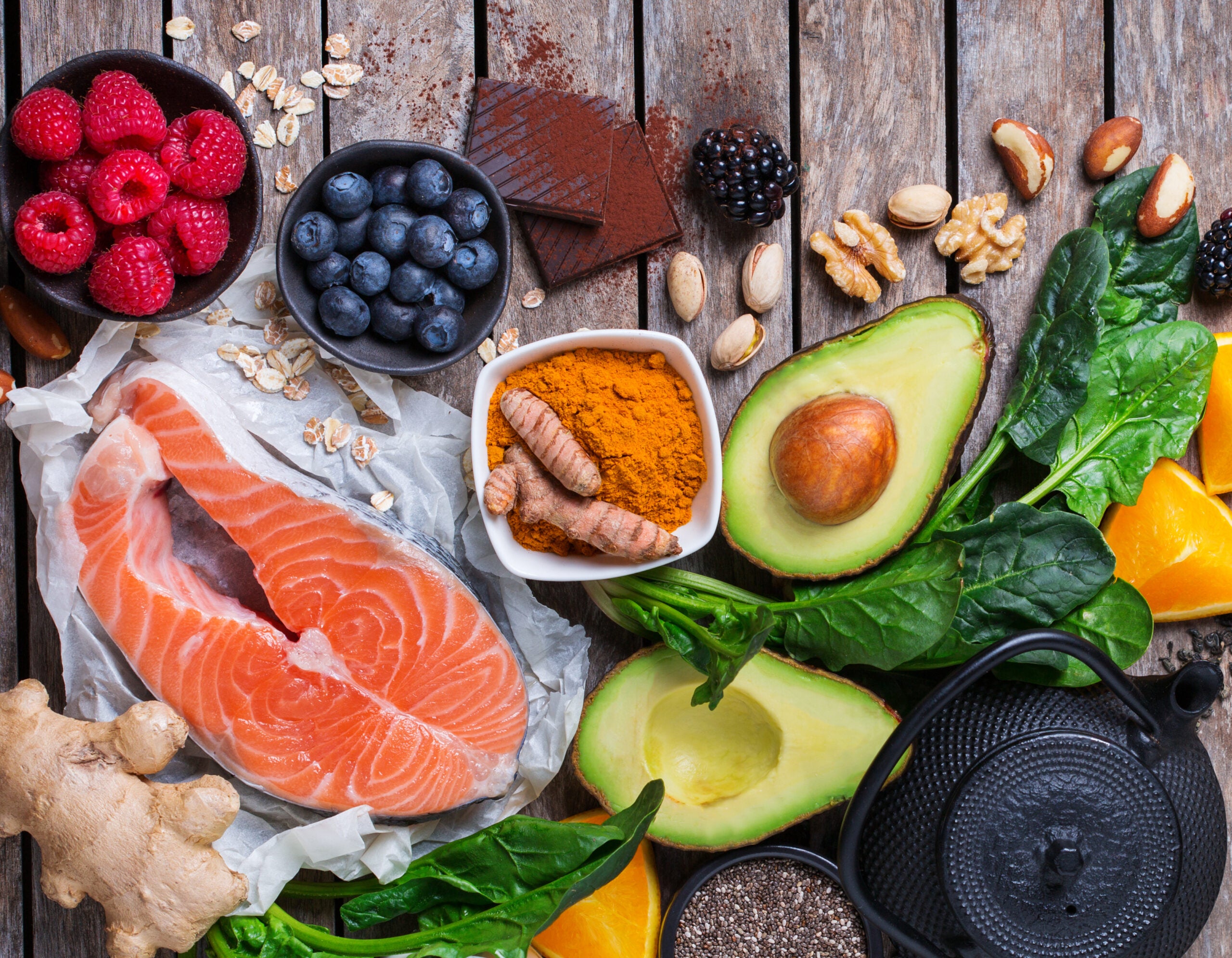 A variety of anti-inflammatory foods including salmon, avocado, turmeric, ginger, dark chocolate, raspberries, blueberries, nuts, seeds, and vegetables, and tea