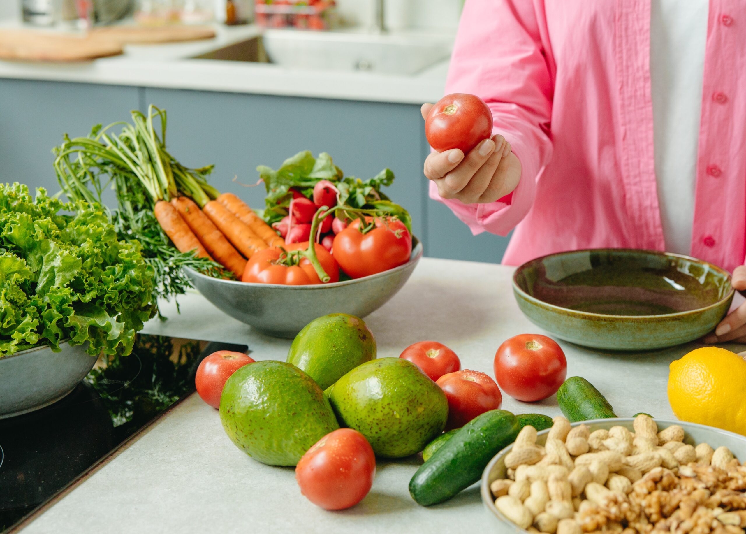 Person in Pink Dress Shirt Holding Red Tomato with a bunch of other colorful produce in the background