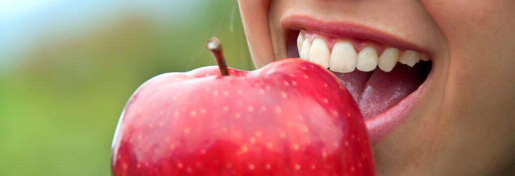 a person with healthy teeth biting into a red apple
