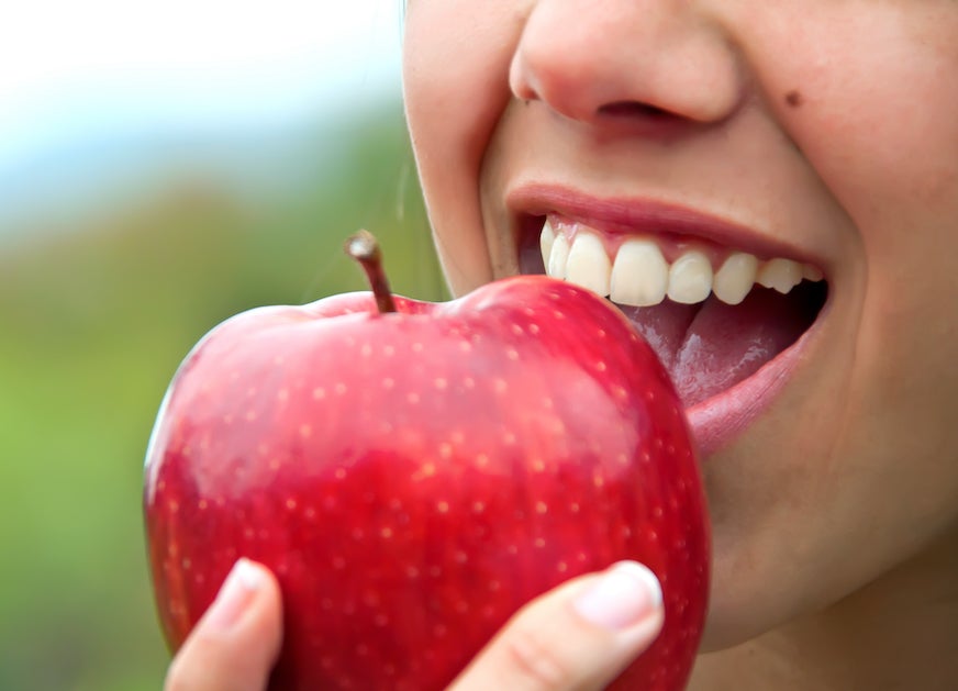 a person with healthy teeth biting into a red apple