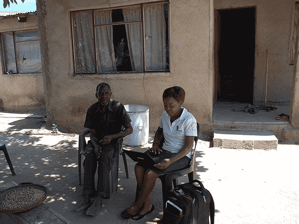 An older South African man and a healthcare worker do an intake sitting outside in rural South Africa
