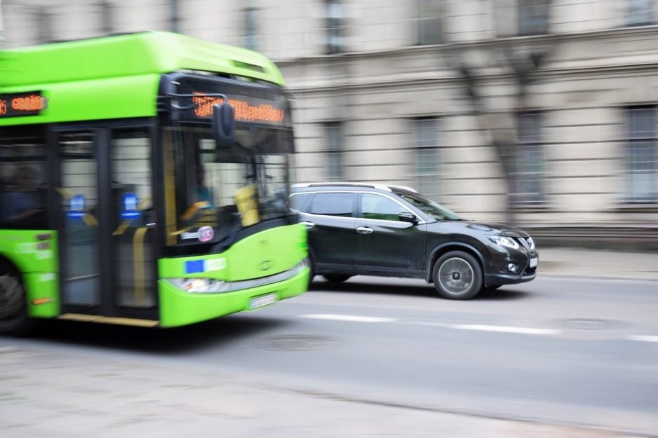 Green bus and a black car driving on a street