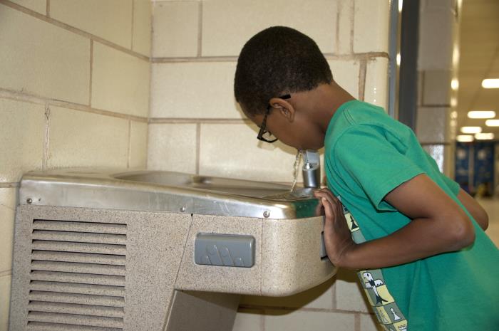 Young boy in green t-shirt drinking from water fountain at school