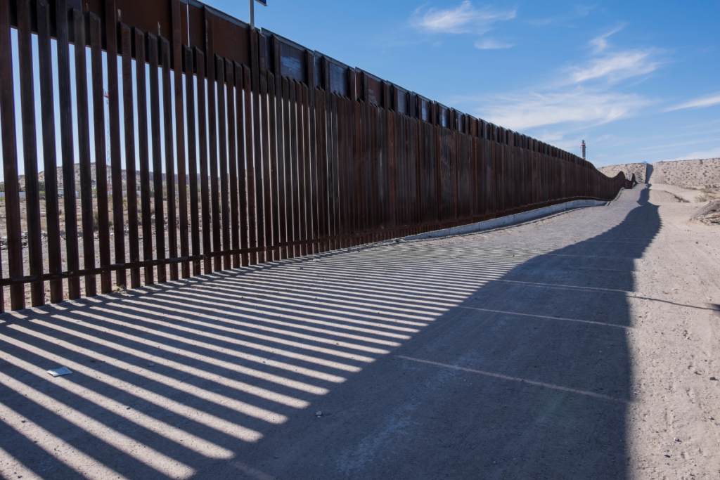 The border fence between New Mexico and Mexico. Strong shadows are cast upon the dirt road on the US side of the border.