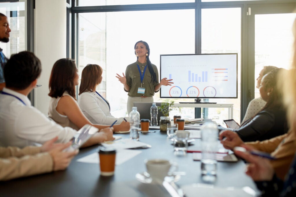 Speaker in front of a graph presenting to a group sitting at a conference table