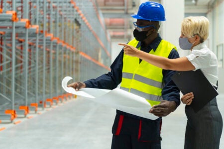 Workers wearing personal protective equipment having a discussion in a warehouse
