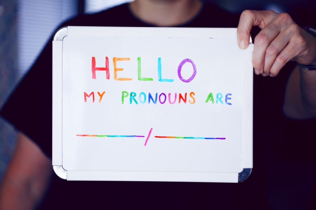 Person holding up a whiteboard that contains the text "Hello my pronouns are ___/____".