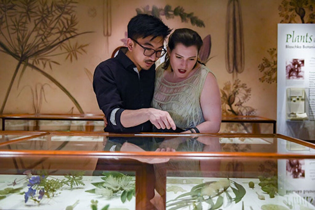a man in black and a woman in green looking down at a glass case