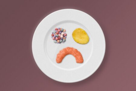 Photo of white plate with M&Ms, a chip, and a cheese curl. The food forms the shape of a face with a frown.