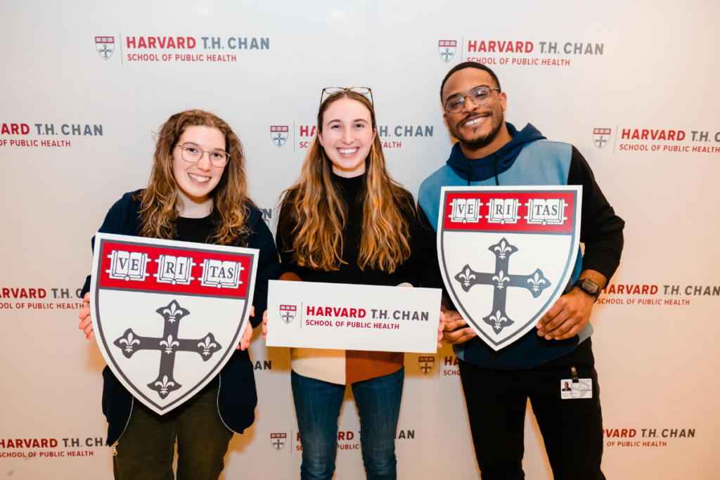 Three Harvard Chan students standing holding veritas logos smiling.
