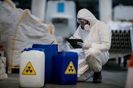 Worker dressed in PPE holding a clipboard inspecting radiological materials