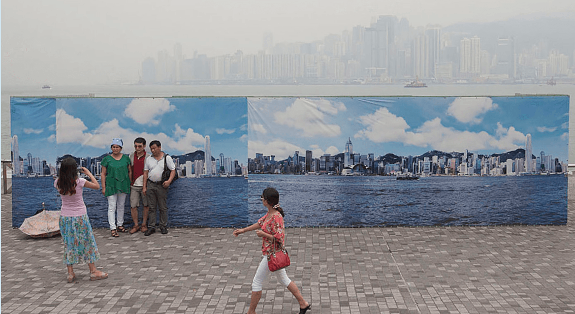Tourists from mainland China pose for photos in front of an outdoor banner picturing what the Hong Kong skyline looks like on a clear day. Air pollution has reached record levels in Hong Kong n recent years, as it has in mainland China.
