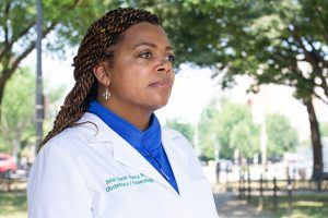 Dr. Joia Crear-Perry, wearing a white doctor's coat, stands outside.