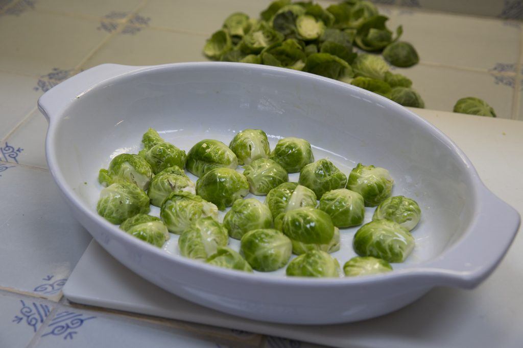 Brussels sprouts coated in olive oil in a roasting dish 