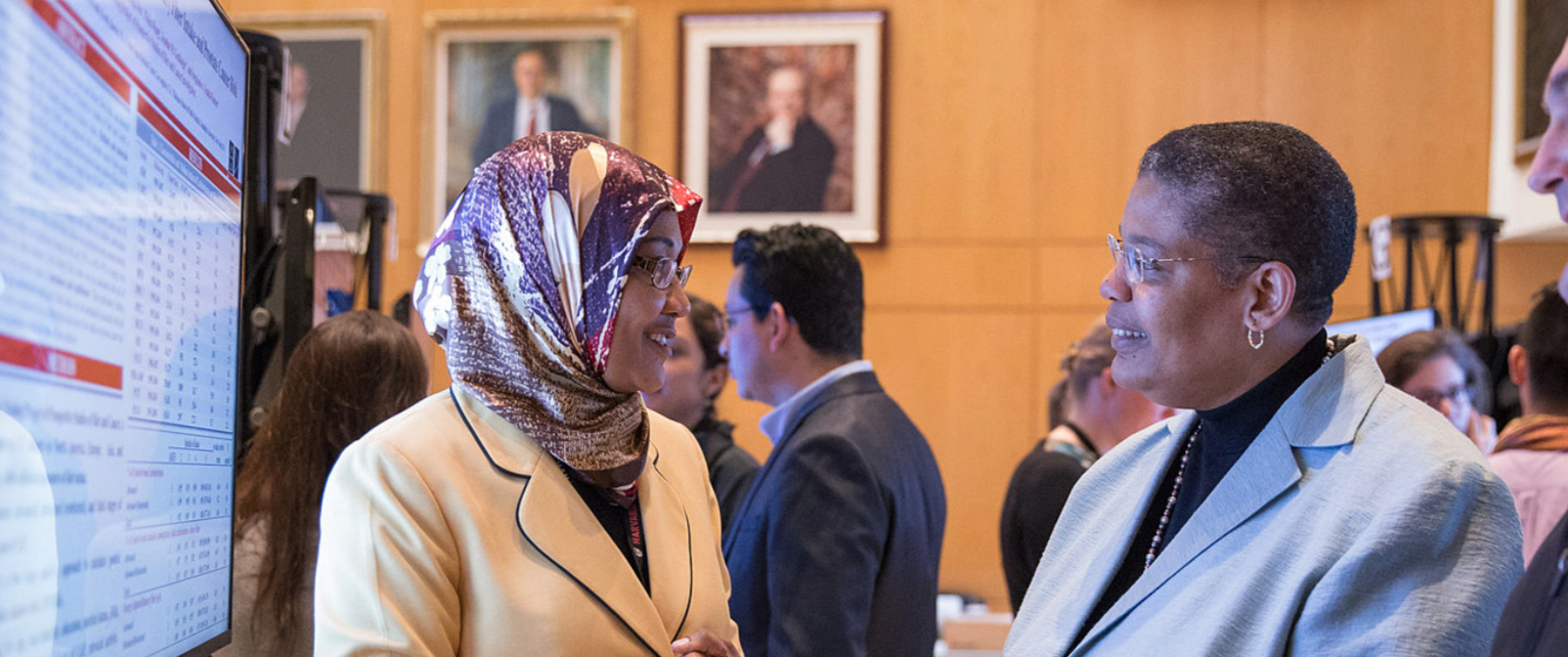 ￼Elkhansa Sidahmed, Yerby Postdoctoral Research Fellow (left), explains her research to Dean Michelle A. Williams at the School’s annual poster day in 2016.
