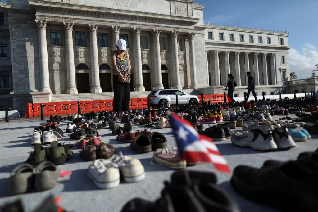 A woman stands among hundreds of pairs of shoes displayed at the Capitol to pay tribute to Hurricane Maria's victims in San Juan